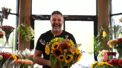 Joyful middle-aged male florist laughing heartily while holding a vibrant sunflower bouquet in his shop
