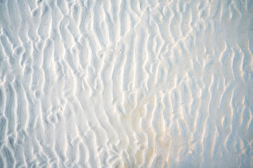 Close-up of beach sand texture with natural wave-like patterns and subtle shadows. Perfect background for summer, vacation, and nature-themed designs or creative projects.
