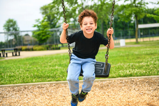 Happy 5 years old boy on a swing. Happy kid on playground