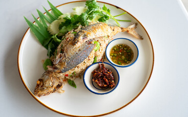 Thai fried rice with mackerel, spicy chili sauce, fresh herbs and cucumber on white plate,...
