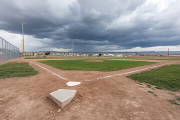 Baseball field dirt infield green grass home plate pitcher mound dramatic sky outdoor sports empty overcast weather