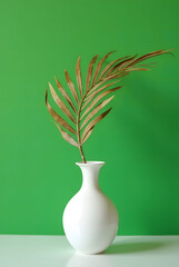 Dried Palm Leaf in White Vase Against Green Background
