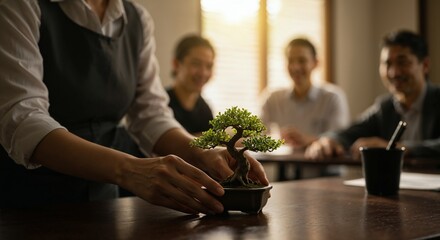 A person carefully places a small bonsai tree on a wooden table during a collaborative business meeting with colleagues in a sunlit office environment