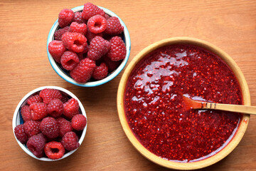 Delicious puree of ripe raspberries in a wooden bowl with a wooden spoon. Ripe raspberries. Flat lay, top view.