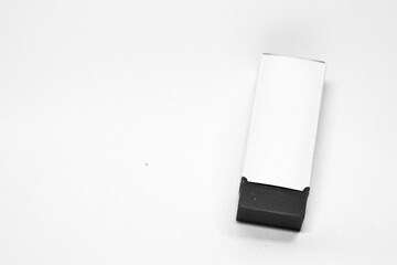 An eraser with a white paper sleeve rests on a white surface, casting a subtle shadow.