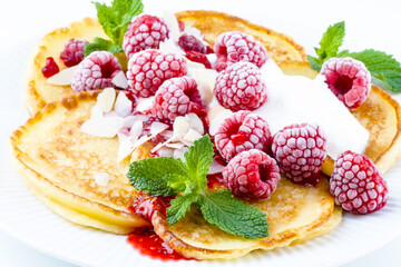 A plate of fluffy pancakes generously topped with fresh raspberries, whipped cream, and sprinkled with almond flakes, mint leaves. Breakfast or sweet dessert concept