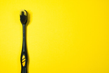 Used black toothbrush with worn bristles on a bright yellow background, positioned to the left.