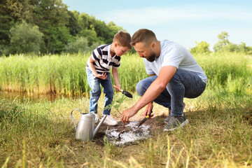 Father and his son planting tree into soil outdoors