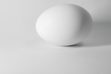 A single, perfectly smooth white sphere rests on a plain white background, subtly illuminated, casting a soft shadow.