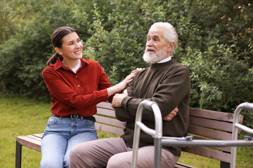 Smiling caregiver supporting elderly man with walking frame outdoors