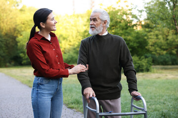 Smiling caregiver supporting elderly man who using walking frame outdoors