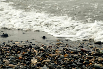 Foamy long sea waves crashing on pebble beach on Black Sea coast at storm. Waves splashing on stones shore in stormy weather. Stormy water surface. Mystical seascape with waves broken on coastline.