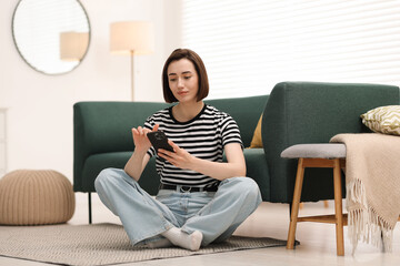 Fototapeta premium Woman using modern smartphone on floor at home
