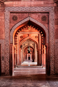 View of a series of ornately decorated reddish arches receding into the distance, creating a mesmerizing tunnel effect, Fatehpur Sikri, Uttar Pradesh, India.