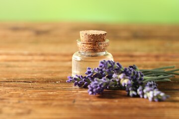 Bottle of lavender essential oil and flowers on wooden table, closeup. Space for text