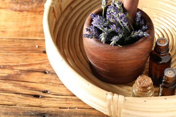Bottles of lavender essential oil and flowers on wooden table, closeup. Space for text