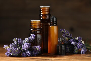 Bottles of lavender essential oil and flowers on wooden table, closeup