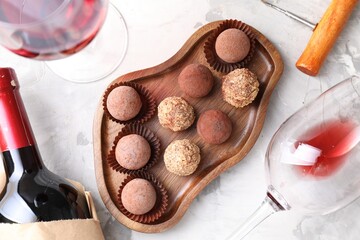 Delicious truffle bonbons and red wine on light grey background, flat lay