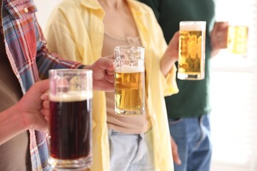 Friends with glass mugs of beer indoors, closeup