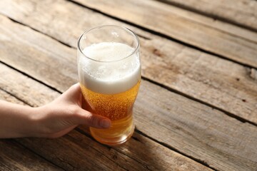 Woman with glass of beer at wooden table, closeup. Space for text