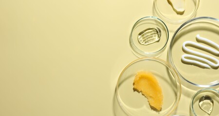 Different cosmetic products in Petri dishes on pale yellow background, flat lay. Space for text