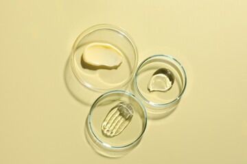 Different cosmetic products in Petri dishes on pale yellow background, flat lay