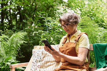 Senior woman enjoys nature in garden while using her smartphone on a sunny afternoon