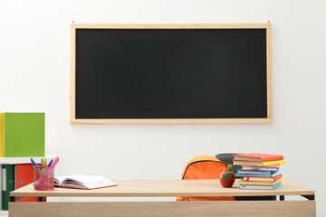 Different stationery and red apple on wooden table near blackboard indoors