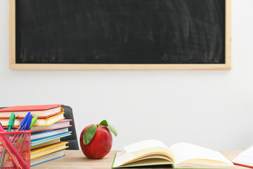 Different stationery and red apple on wooden table near blackboard indoors, closeup