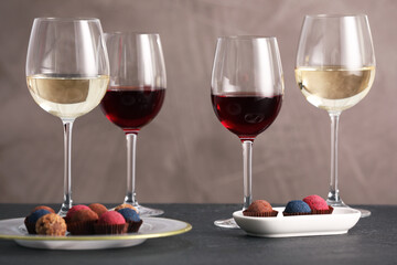 Delicious truffle bonbons and wine on black table against grey background