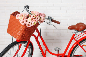 Bicycle with basket of beautiful flowers near white brick wall indoors, closeup