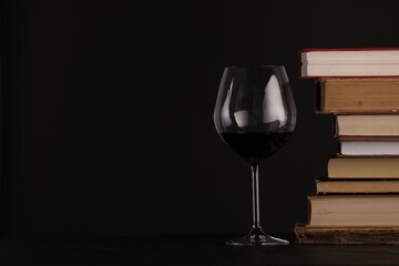 Red wine in glass and stack of books on table against black background, closeup. Space for text