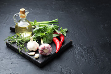 Different fresh herbs and spices on black table, space for text