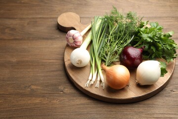 Different fresh herbs, onions and garlic on wooden table, closeup. Space for text