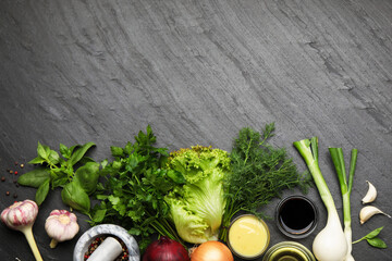 Different aromatic herbs, sauces, products and peppercorns on dark textured table, flat lay. Space...