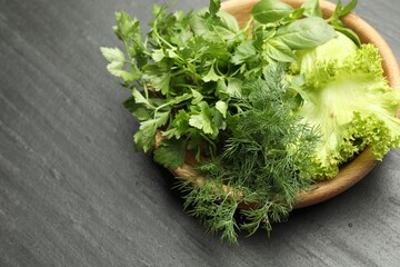 Different aromatic herbs in bowl on dark textured table, closeup. Space for text