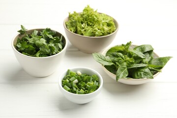 Different aromatic herbs in bowls on white wooden table, closeup