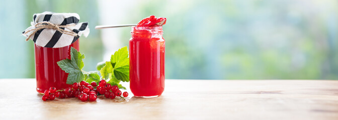Fresh homemade red currant jam in jar with fresh picked currants on table against light bokeh background. Horizontal close-up with space for text.