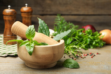 Different aromatic herbs in mortar and spices on wooden table, closeup