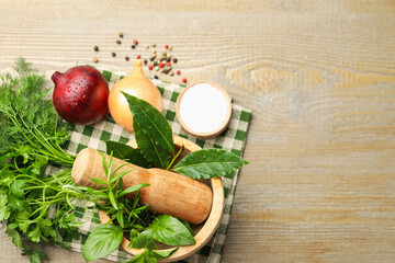 Different aromatic herbs in mortar, onion and spices on wooden table, flat lay. Space for text