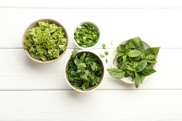 Different aromatic herbs in bowls on white wooden table, flat lay