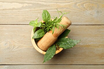 Different aromatic herbs in mortar on wooden table, top view