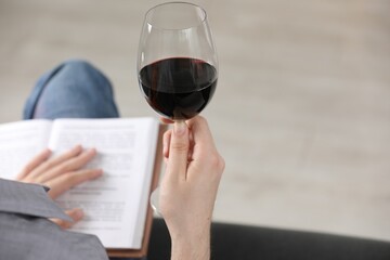 Woman with glass of wine reading book on sofa at home, closeup. Space for text