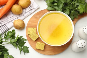Aromatic bouillon cubes, broth, parsley and vegetables on white marble table, flat lay