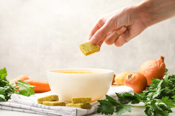 Woman putting aromatic bouillon cube into broth at table, closeup