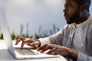 Astonished male employee typing quickly on laptop and looking at screen with surprised expression