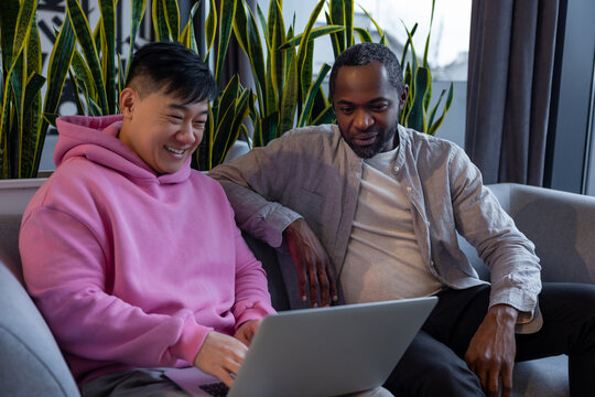 Two diverse male colleagues sitting on couch and discussing project on laptop