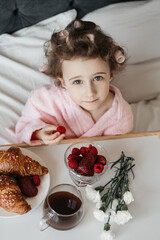 
A child with curlers in her hair, wearing a pink bathrobe, smiles cheerfully while enjoying...