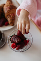 
A child with curlers in her hair, wearing a pink bathrobe, smiles cheerfully while enjoying...