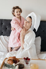 A loving moment between an adult woman and a child in bathrobes, facing each other on a bed, with a...